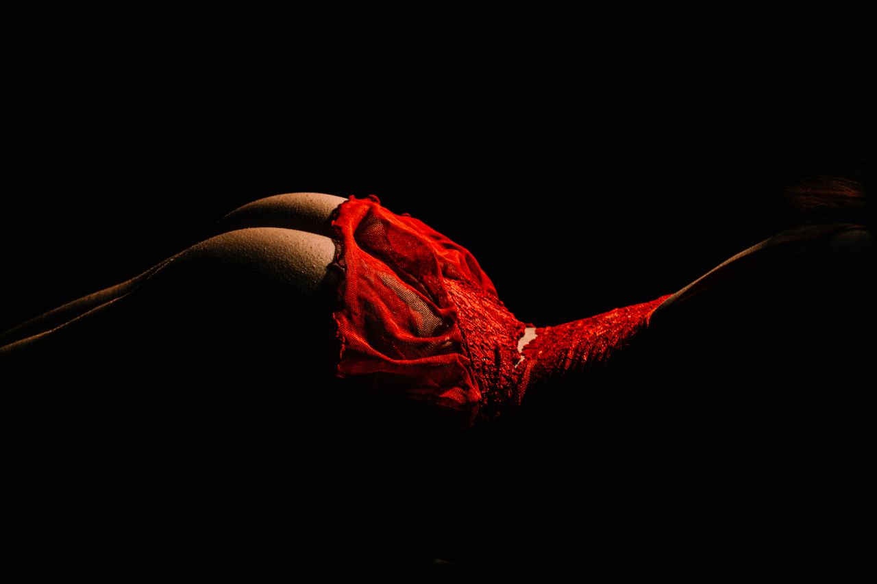Home Striking studio shot of a woman posing in red lingerie against a dark background.